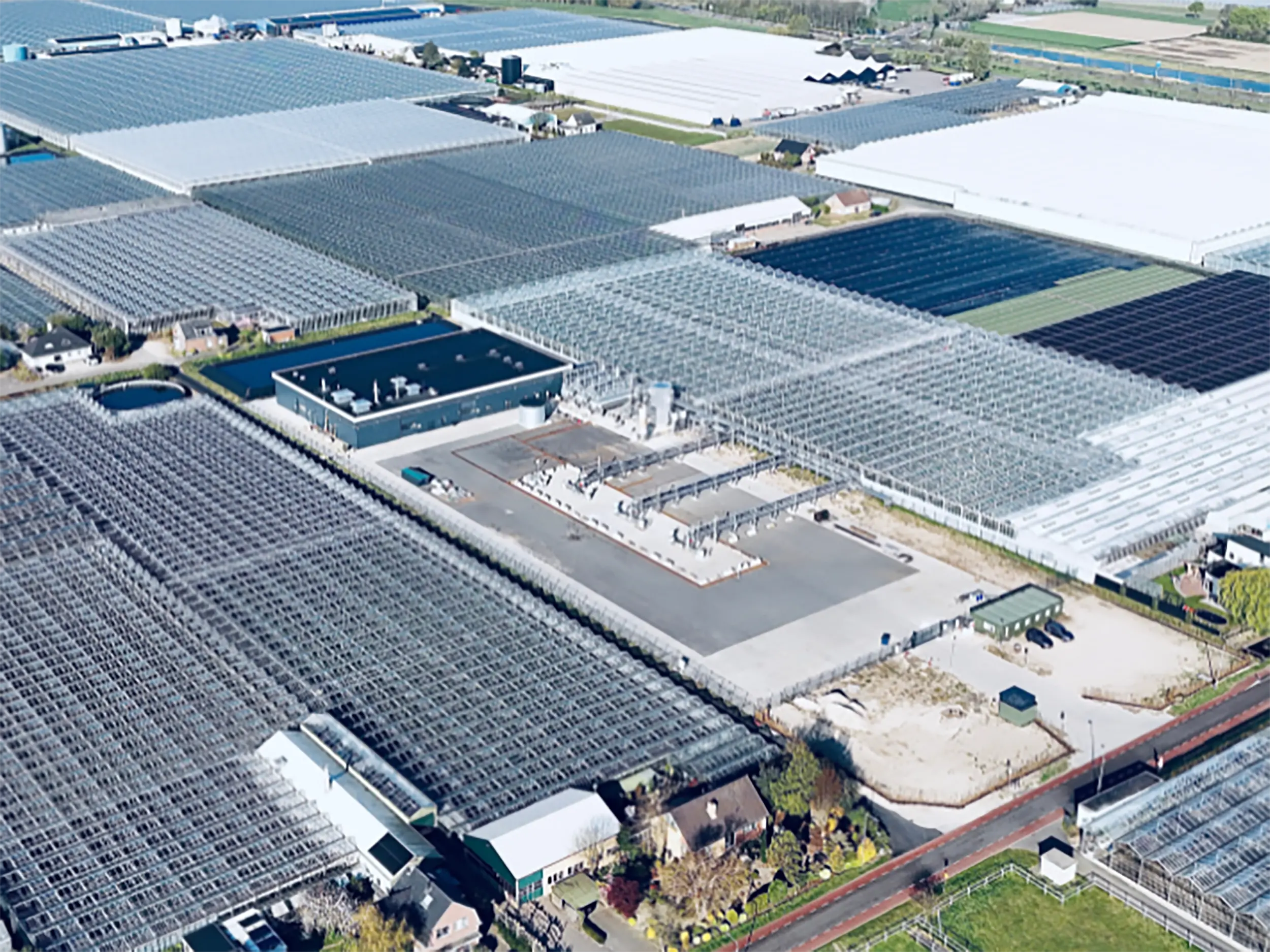 aardwarmtecluster-maasdijk-tussen-kassen Luchtfoto van een groot glastuinbouwgebied in Maasdijk met kassen en een centraal aardwarmtecluster tussen de kassen.